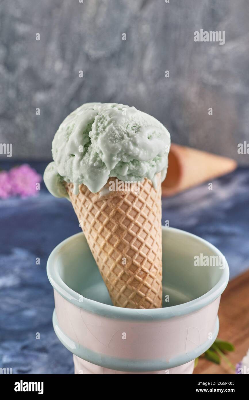 Gelato al pistacchio nel cono del waffle e vase su sfondo blu Foto Stock