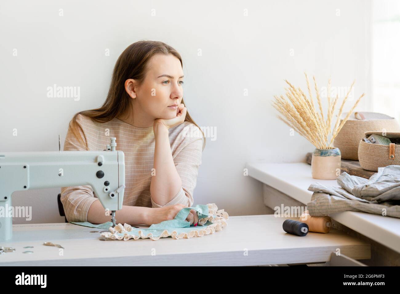 Giovane donna d'affari seduto sul suo posto di lavoro in atelier cucito e guardando in finestra Foto Stock