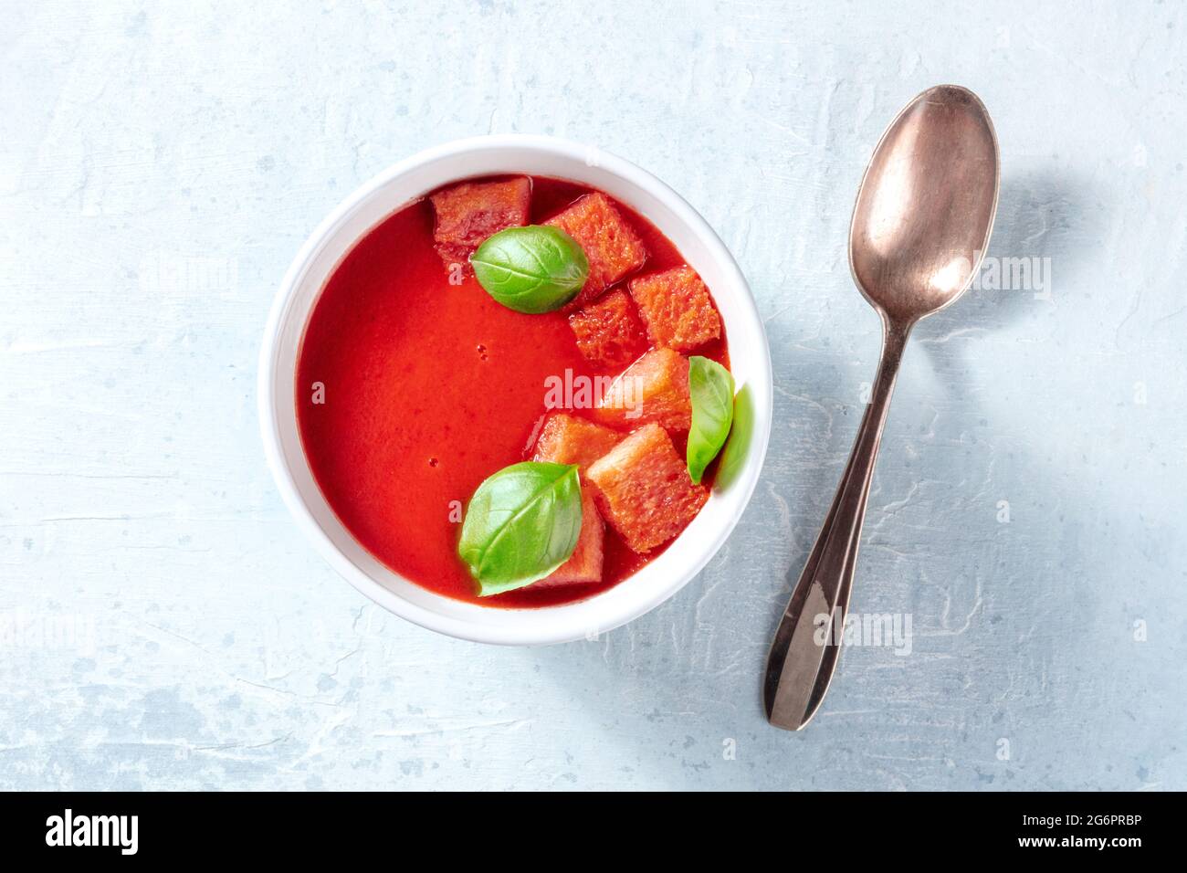 Zuppa di pomodoro vegana con basilico fresco, sparata dall'alto con un cucchiaio su un tavolo di ardesia grigia Foto Stock