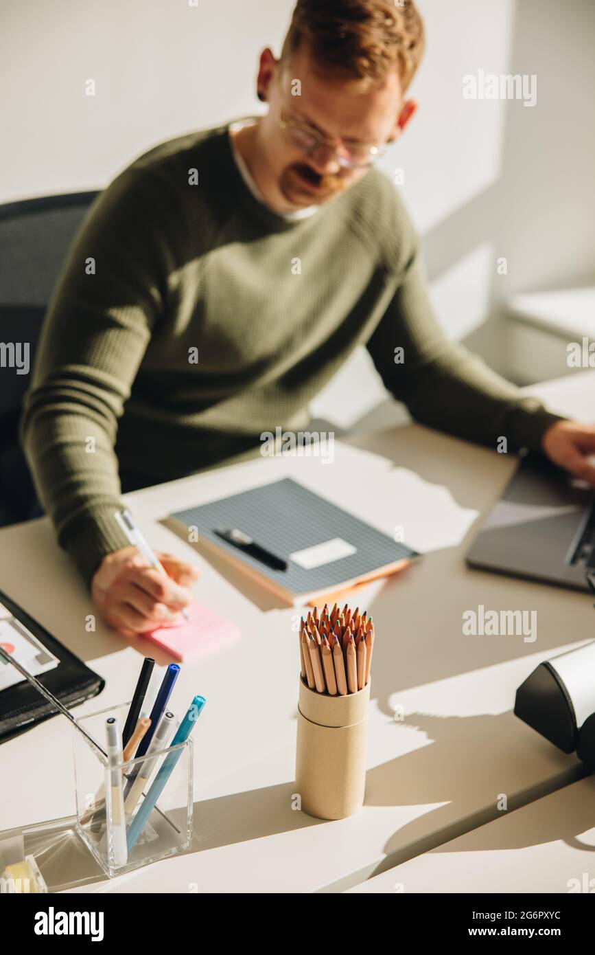 Uomo che prende appunti mentre lavora su un notebook. uomo d'affari che ha annotato alcuni punti importanti su un appiccicoso. Foto Stock