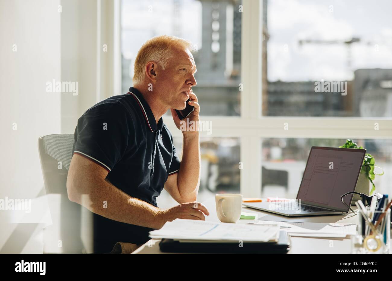 Uomo d'affari senior che parla al telefono. Office Manager effettua una chiamata mentre è seduto alla scrivania. Foto Stock