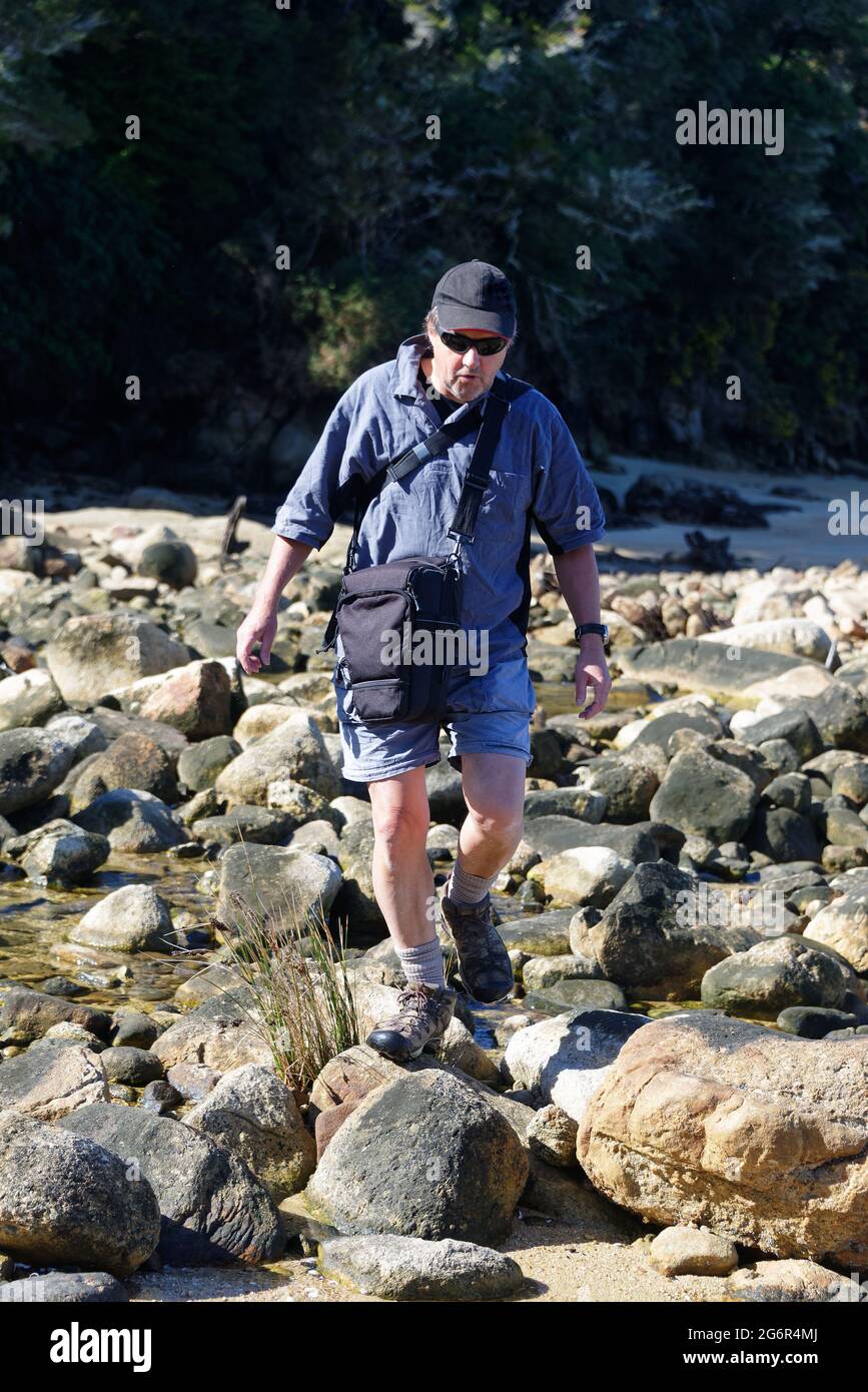 Un uomo anziano sta saltando attraverso le rocce sulla costa Foto Stock