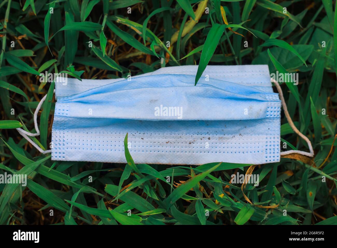 Maschera chirurgica usata, maschera chirurgica gettata sull'erba, inquinamento ambientale e le conseguenze di un uso eccessivo di maschere chirurgiche durante il coronavirus. Foto Stock