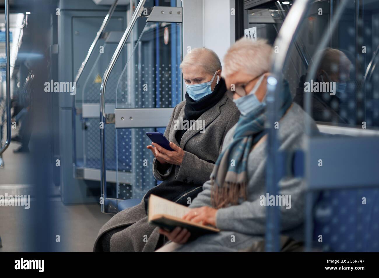 due passeggeri maturi in maschere protettive seduti in un'auto metropolitana. regole della città durante la pandemia. Foto Stock