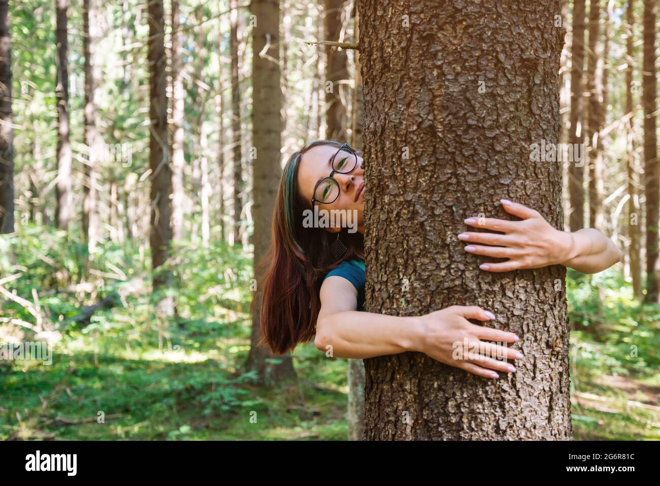 Giovane donna allegra abbracca un albero in un parco o in una foresta. Foto Stock