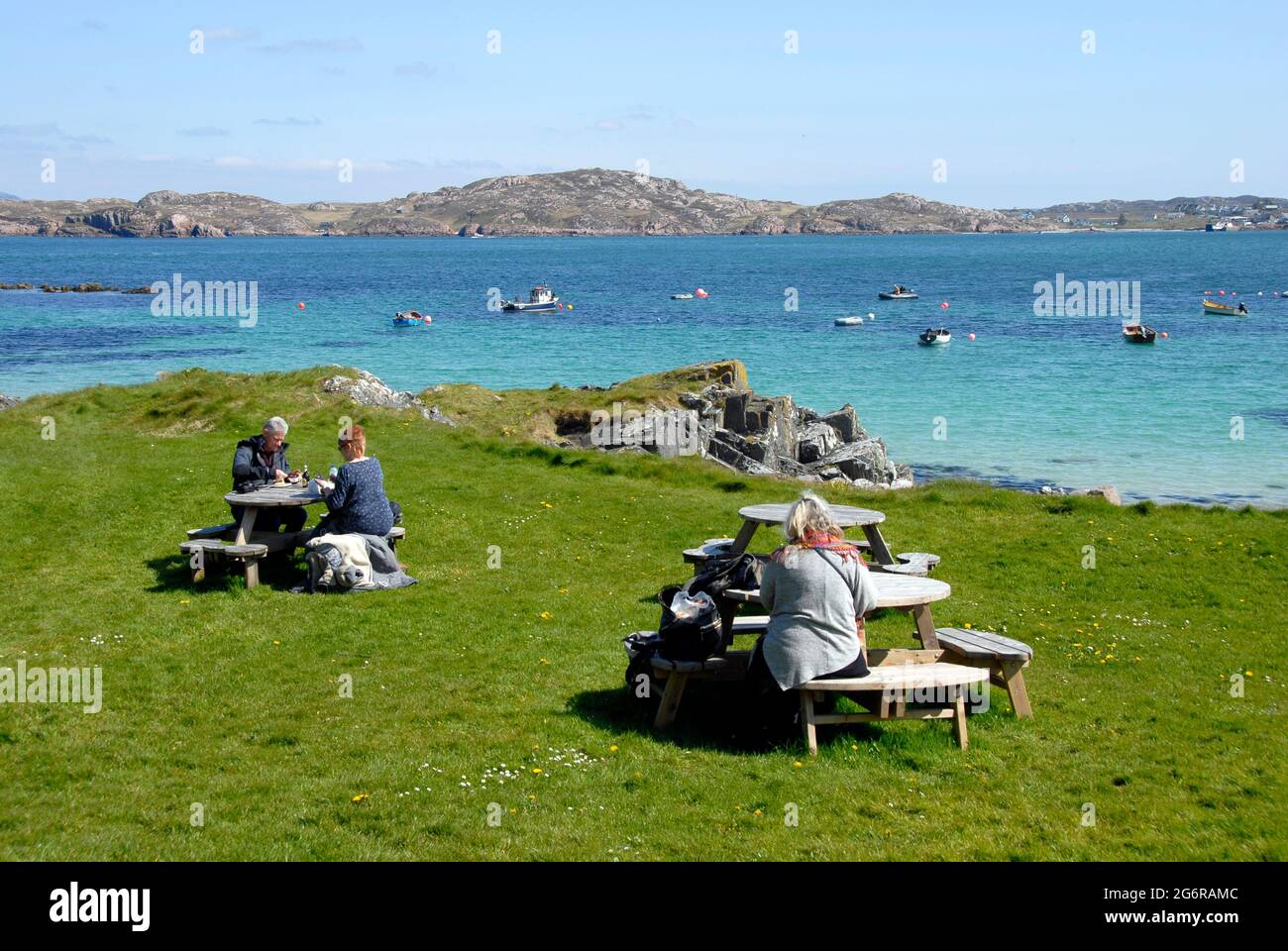 Le persone che hanno rinfreschi all'aperto accanto al breve tratto d'acqua che separa Iona da Mull, Iona, Scozia Foto Stock