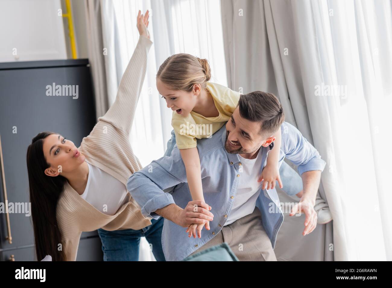 donna che imita piano mentre eccitato figlia piggybacking sul retro di papà Foto Stock