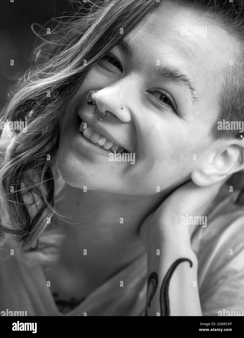 Un ritratto di una giovane donna che sorride e si appoggia la testa sulla mano mentre guarda la fotocamera. Foto Stock