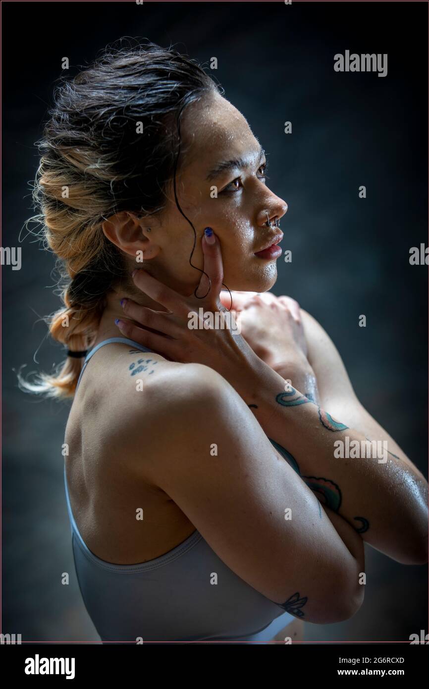 Vista laterale di una giovane donna con tatuaggi in abiti sportivi, la testa sta poggiando sulle braccia. Sta guardando in su mentre il sudore si fa travolgire giù la sua faccia. Foto Stock