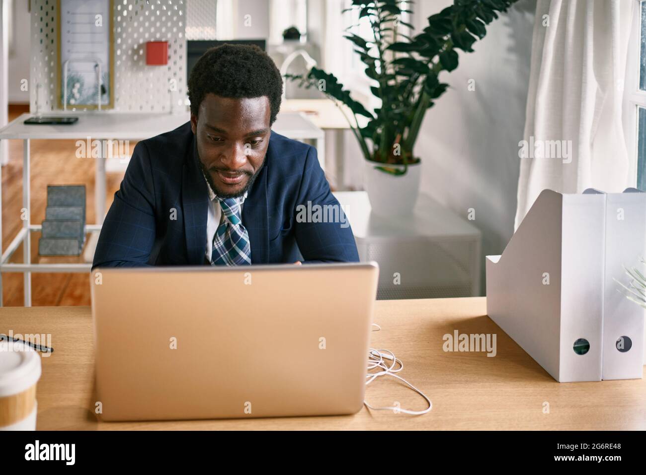 Giovane uomo africano che lavora su computer portatile all'interno di un ufficio moderno - Focus on Face Foto Stock