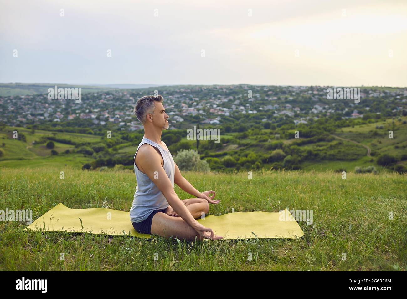 Yoga. Un uomo con capelli grigi pratica la meditazione sulla natura in estate. Foto Stock