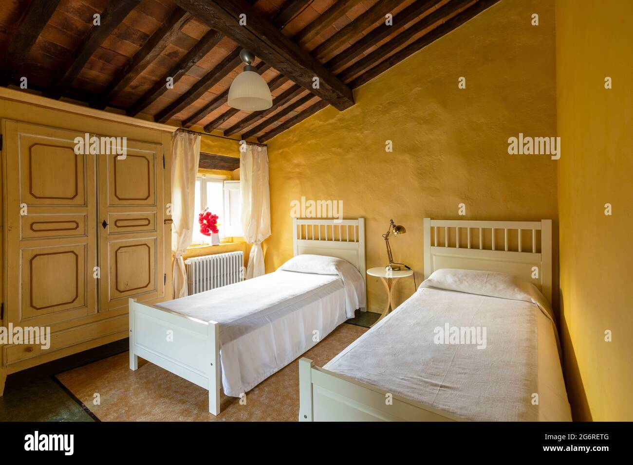 Interno di una camera da letto con due letti singoli. Atmosfera spartana e niente di lussuoso. Le pareti sono gialle ed è un'antica casa italiana toscana Foto Stock