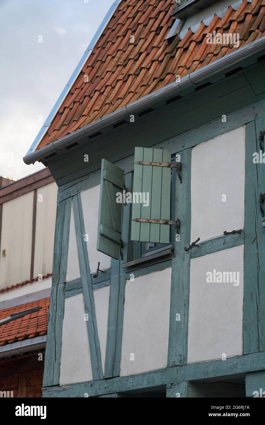 Particolare di una parete di casa a graticcio con finestra, ferramenta e persiane a mezza apertura in bianco, verde e grigio. Tegole rosse sul tetto. Klaipeda, L. Foto Stock