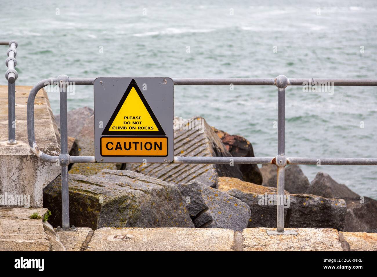 Un cartello di fronte alle rocce sulla costa leggere attenzione si prega di non salire su rocce Foto Stock
