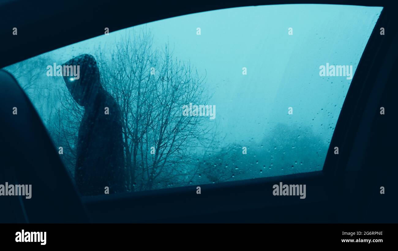 Un concetto horror. Guardando in su attraverso una finestra dell'automobile ad un'entità soprannaturale spaventosa con gli occhi luminosi, camminando oltre un automobile. Su una moody inverni sera. Foto Stock