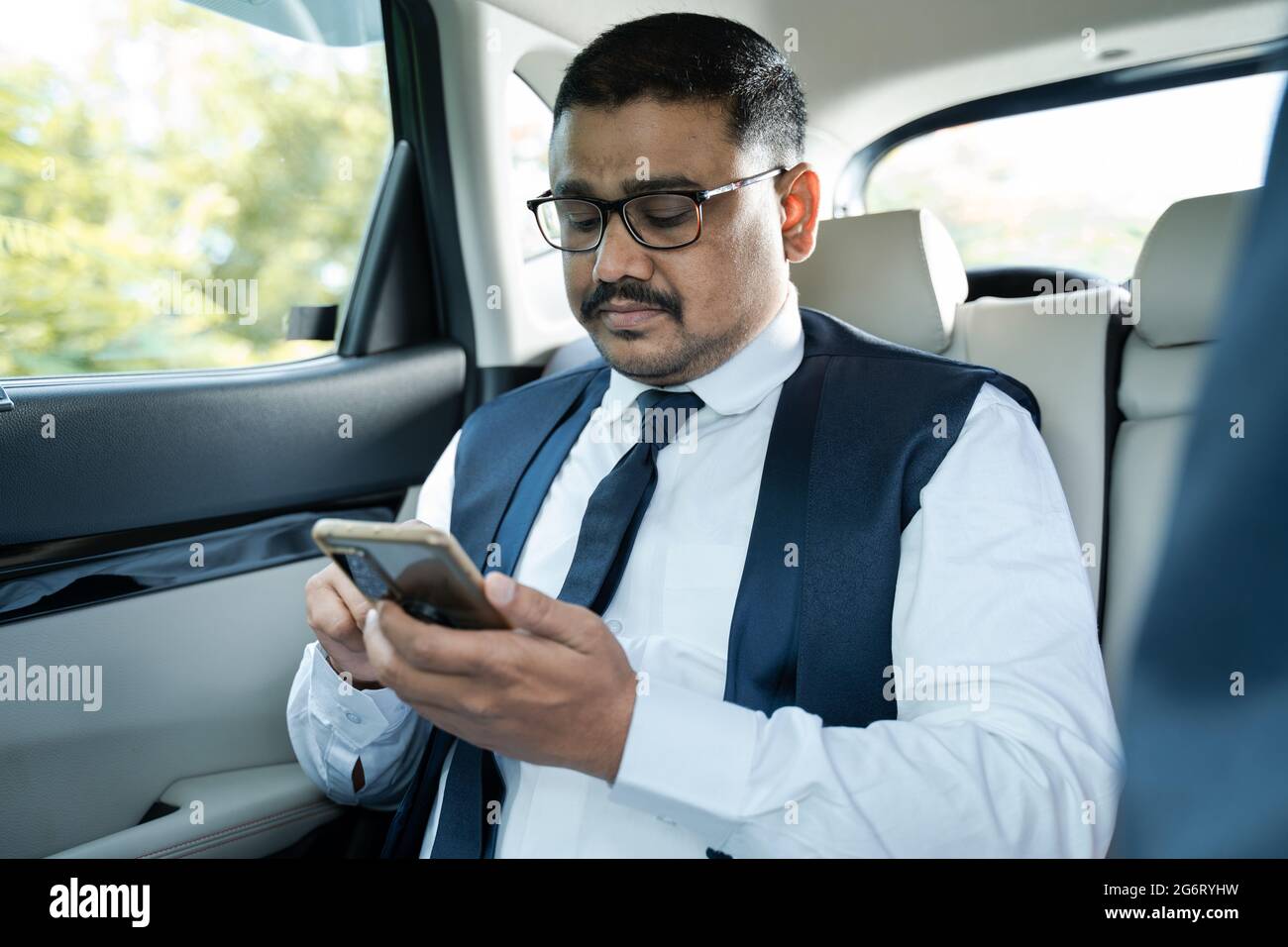 Giovane uomo d'affari occupato utilizzando il telefono cellulare su auto in movimento - concetto di persone di successo, tecnologia e felicità. Foto Stock