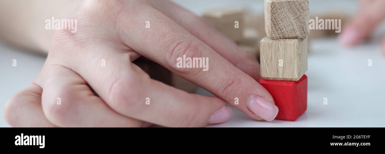 Mano femmina che estrae il cubo di legno rosso dalla base di torre closeup Foto Stock