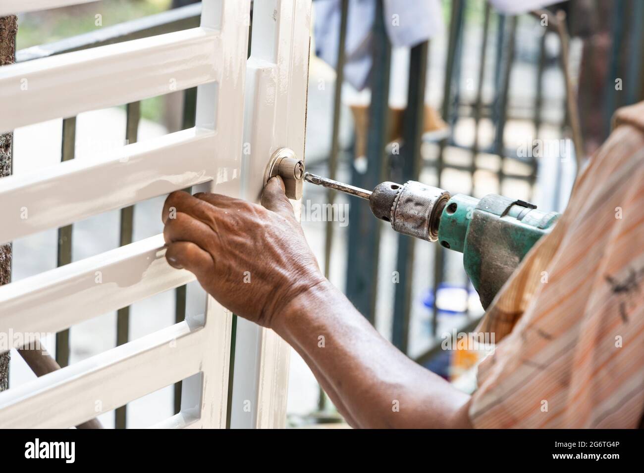 Operatore che monta la nuova porta della griglia metallica sull'edificio residenziale con un cacciavite elettrico Foto Stock