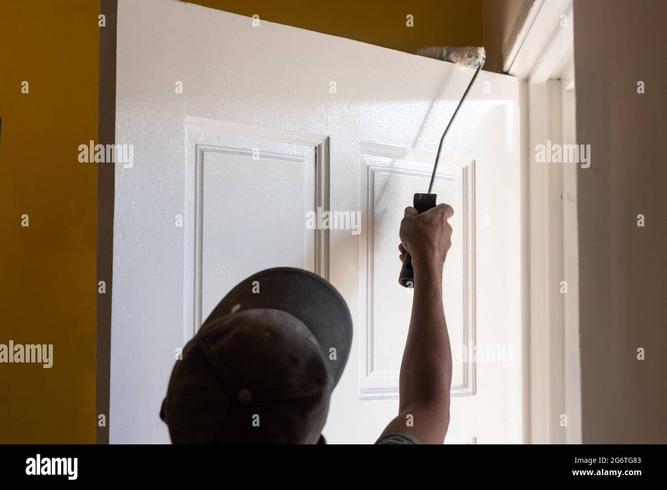 Persona che dipinge porta bianca di legno con rullo di vernice durante la rinovazione domestica. Sfocatura del movimento prevista. Foto Stock