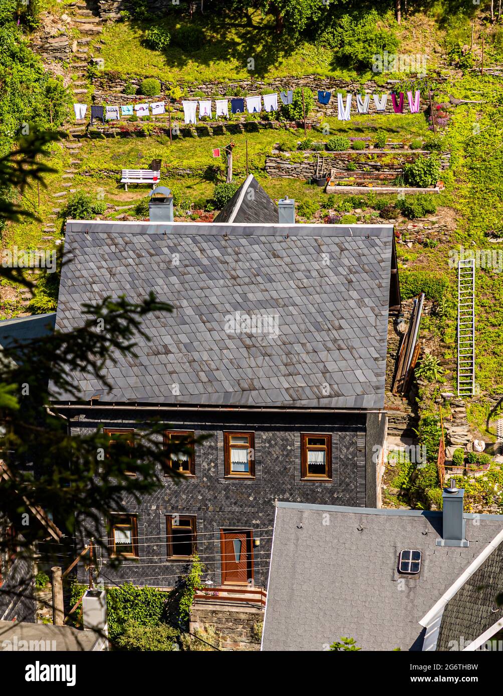 Lavatrici colorate sono appese a una corda nel giardino terrazzato sopra una casa rivestita di ardesia sul pendio di Lauscha, Turingia, Germania. La città è considerata la culla della decorazione natalizia in vetro soffiato a mano dalla fondazione della sua vetreria da parte di Hans Greiner e Christoph Müller nel 1597. Foto Stock