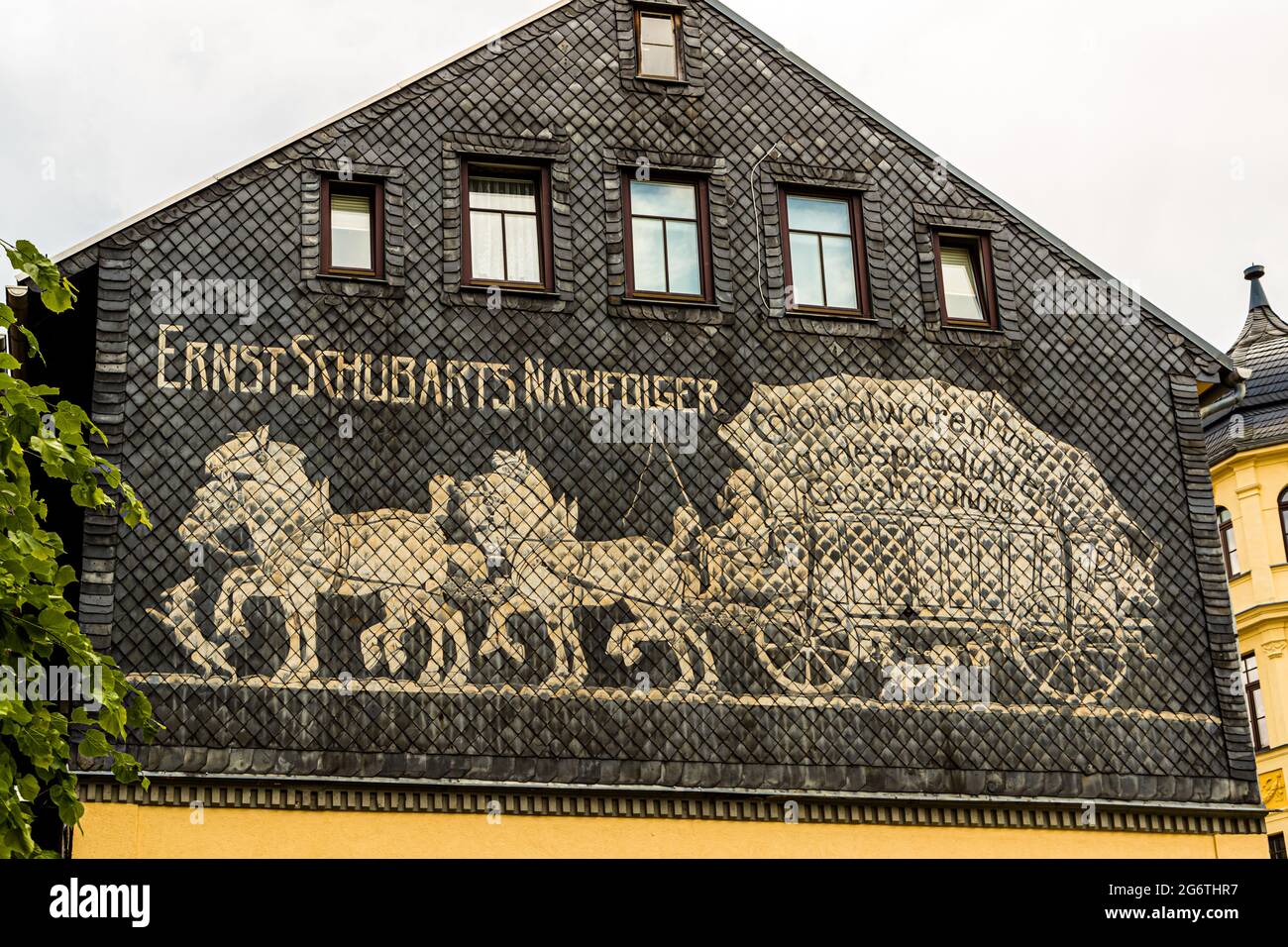 Un murale storico sulla facciata rivestita di ardesia di una casa a Sonneberg, Turingia, Germania, raffigura un carro di consegna trainato da quattro cavalli e la scritta "Ernst Schubarts Nachfolger" ("Il successore di Ernst Schubart"). Scritte aggiuntive, parzialmente oscurate, indicano un'ex attività di drogheria e prodotti vari una volta situata qui. Foto Stock