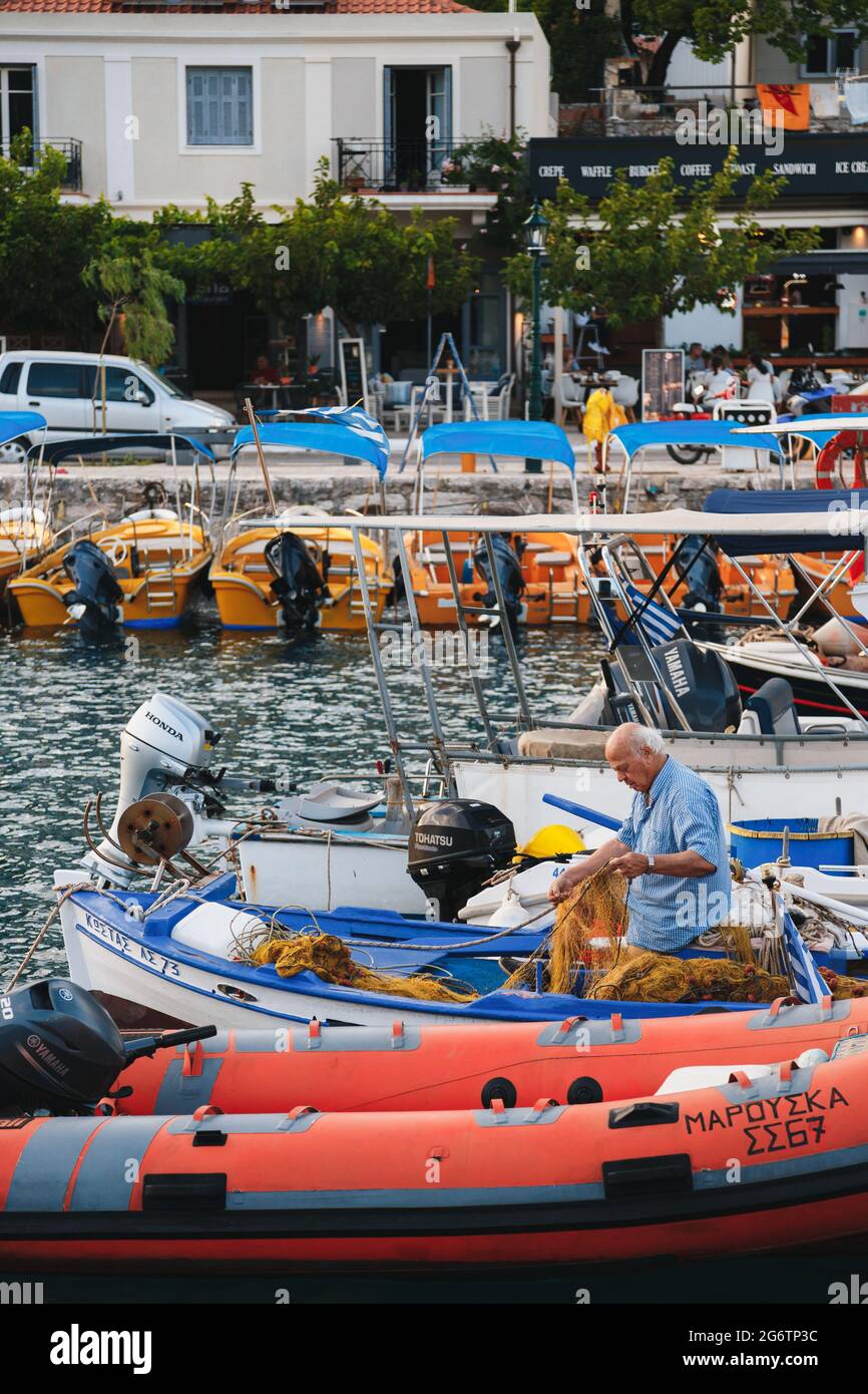 Agia Efimia, isola di Cefalonia, Grecia - Luglio, 12 2019: Un vecchio pescatore greco seduto in una boad e preparando una rete da pesca per la prossima pesca. Foto Stock