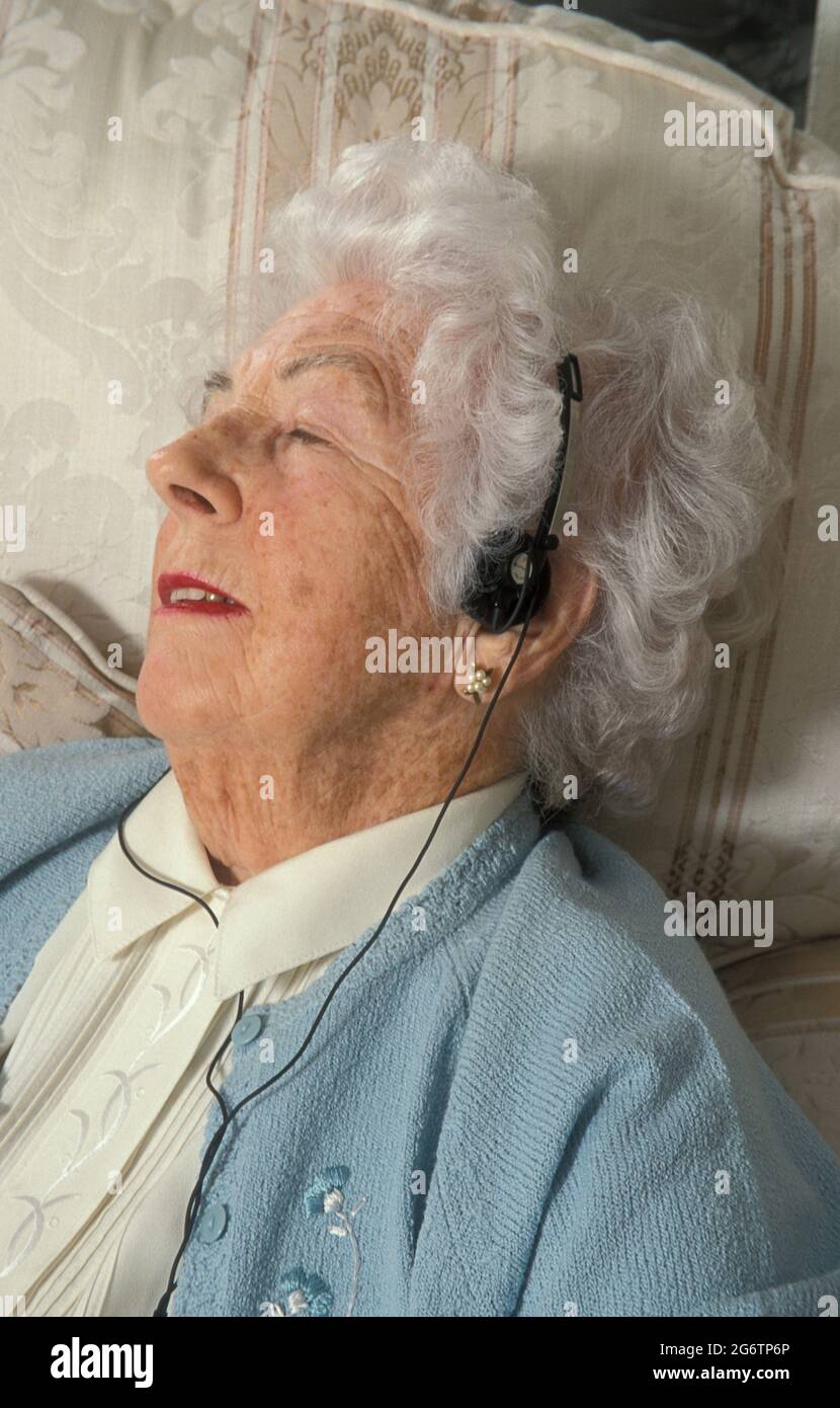 donna anziana che si rilassa in poltrona ascoltando la musica con le cuffie Foto Stock