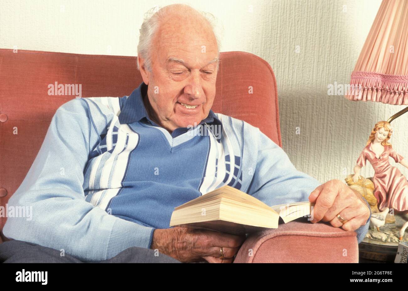 uomo anziano in poltrona leggere un libro Foto Stock
