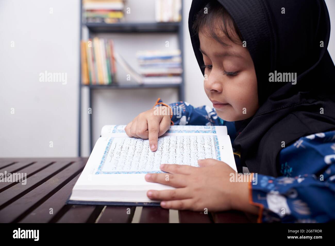 Bambina asiatica che legge Koran dopo aver pregato a casa Foto Stock