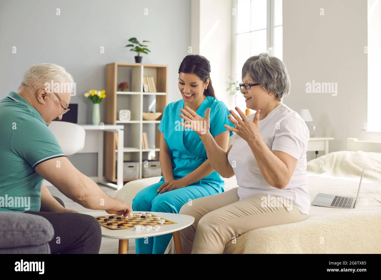 Felice coppia senior in pensione e la loro infermiera giocando a scacchi e divertendosi insieme Foto Stock