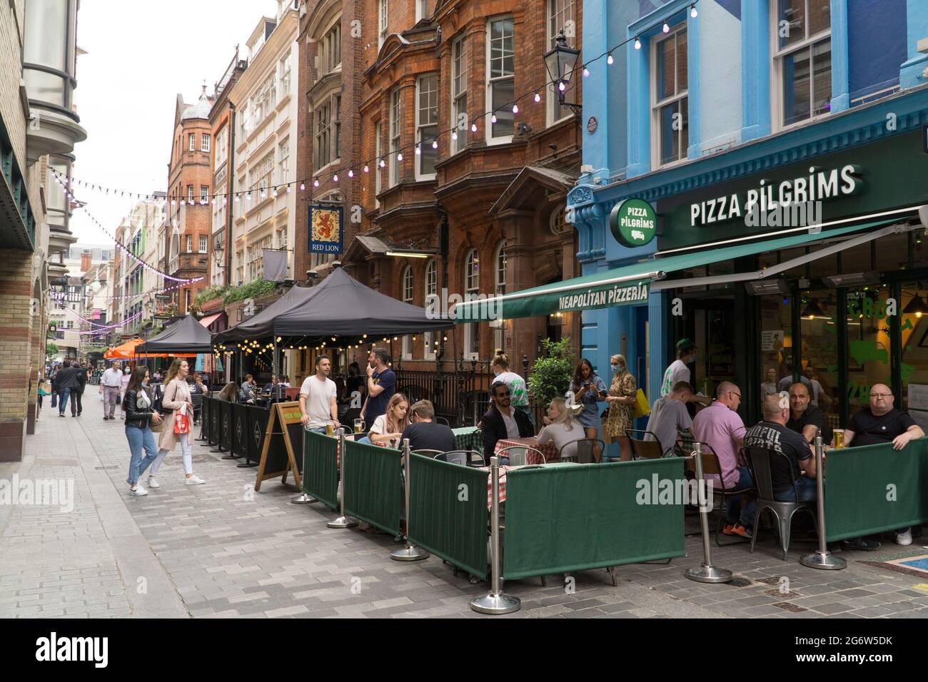 Londra, Regno Unito, 8 luglio 2021: La ristorazione all'aperto rimane l'opzione preferita per molte persone in quanto i casi crescenti della variante Delta causano preoccupazione. A Kingly Court, appena fuori da Carnaby Street di Londra, i commensali e i bevitori possono divertirsi sapendo che uno spazio molto ben ventilato riduce i rischi di trasmissione del coronavirus. I grandi ombrelloni proteggono dalla pioggia e dal sole, che sono entrambi abbastanza probabili in qualsiasi giorno estivo inglese. Anna Watson/Alamy Live News Foto Stock