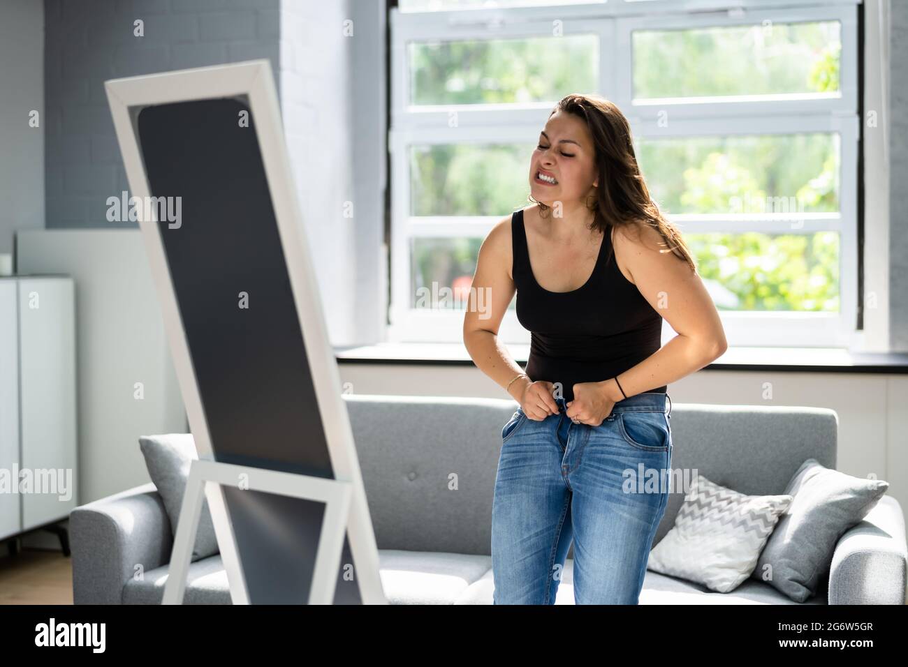 Donna che lotta con jeans stretti. Guadagno peso Foto Stock