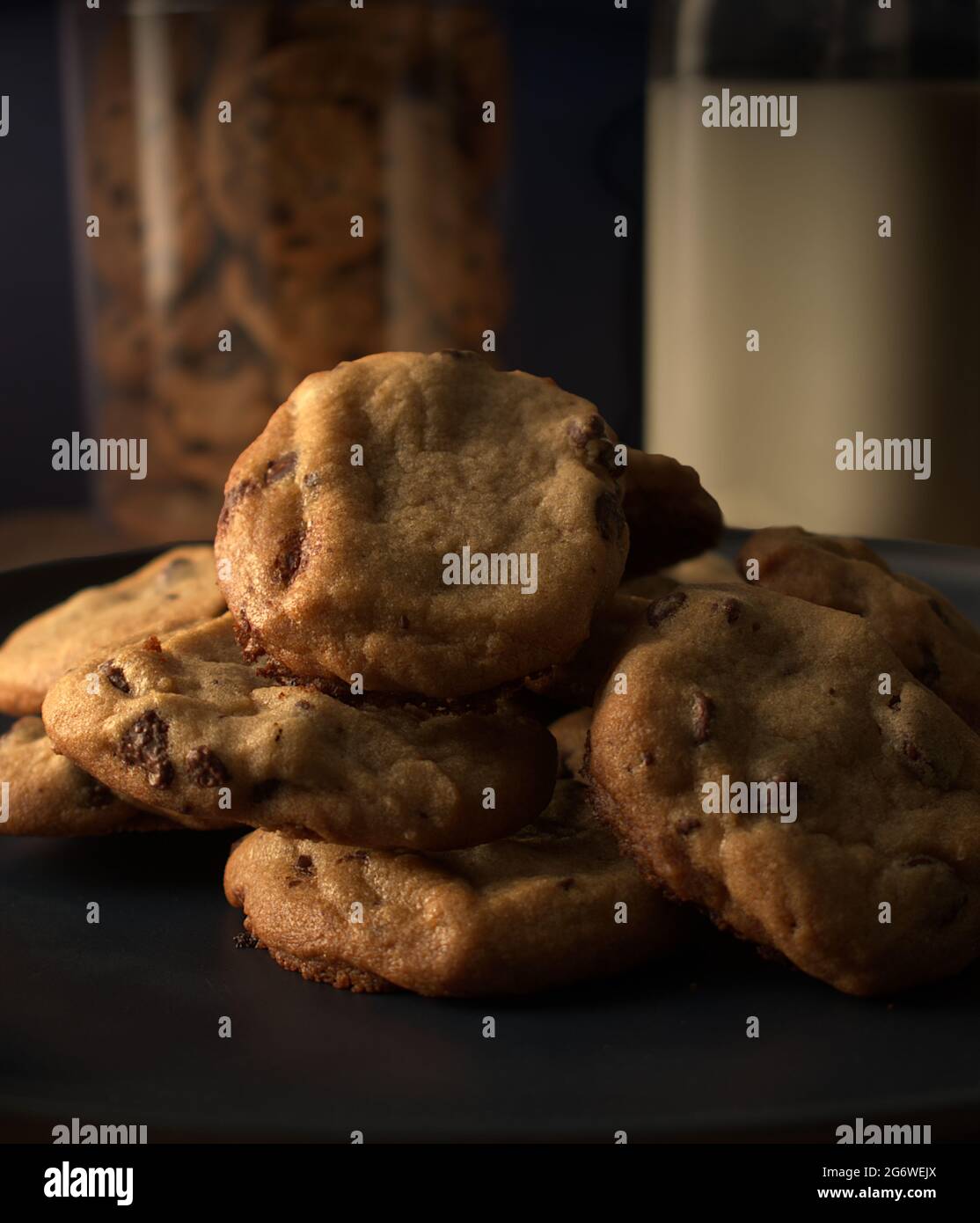 Biscotti appena fatti visualizzati su un piatto blu scuro. Dietro il piatto si trova un vasetto di biscotti a sinistra e a destra una caraffa di latte Foto Stock