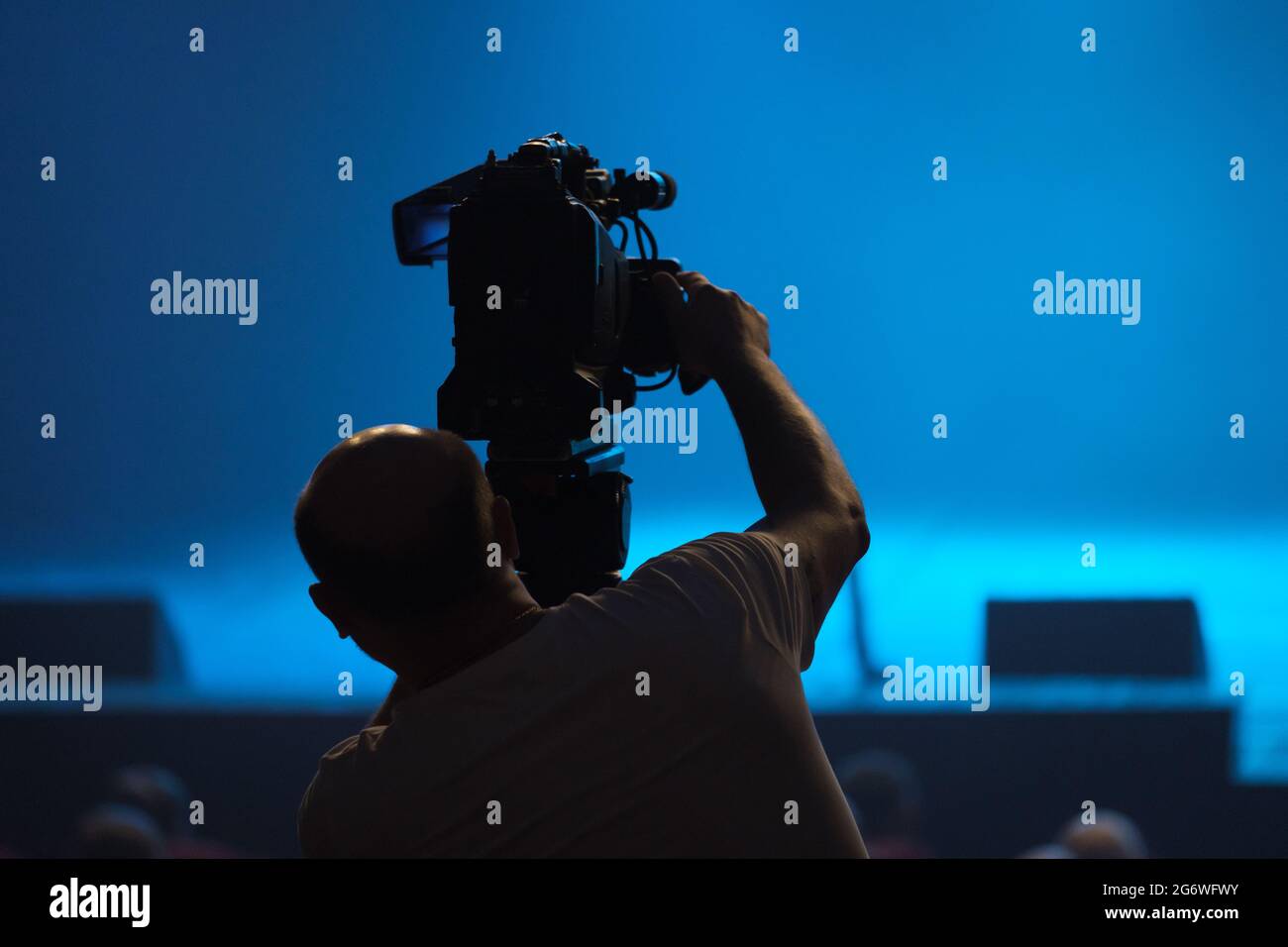 Silhouette di un cameraman con una videocamera impegnata in riprese video nella sala. Foto Stock