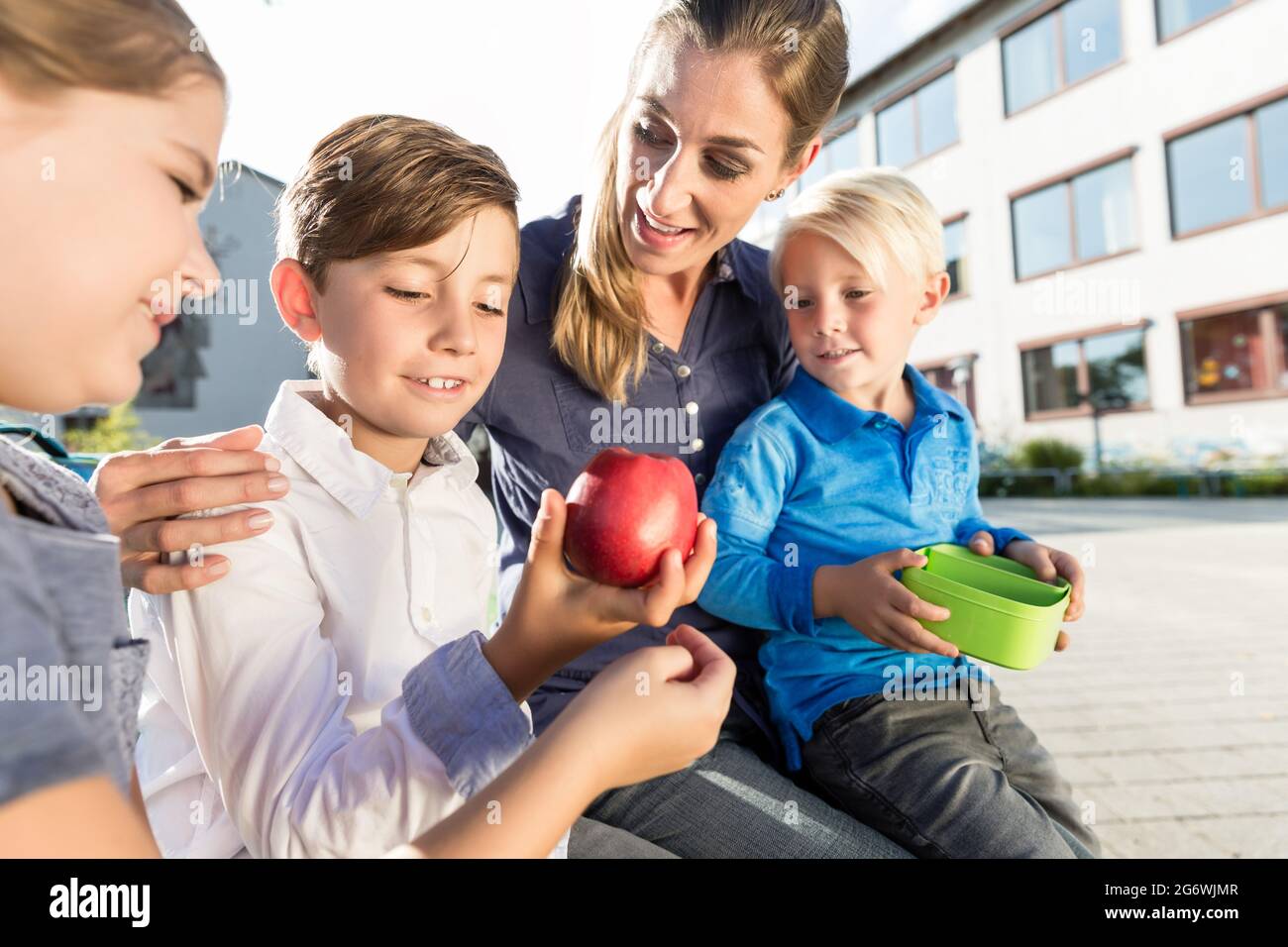 Madre e bambini a scuola con pausa con mela e scatola per il pranzo Foto Stock