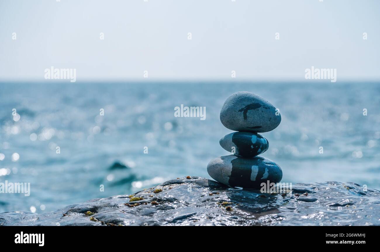 Equilibrata piramide di ciottoli sulla spiaggia in una giornata di sole. Abstract Sea bokeh sullo sfondo. Messa a fuoco selettiva. Pietre Zen sulla spiaggia di mare, meditazione Foto Stock