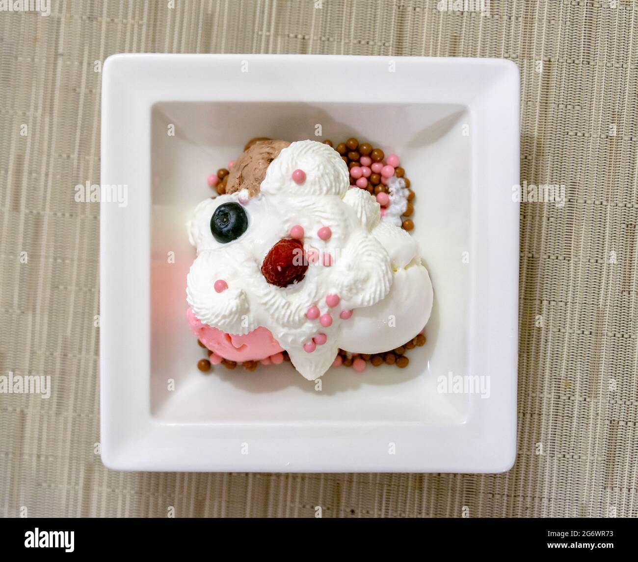 Vista dall'alto della vaniglia e del gelato alla fragola con panna montata e frutti di bosco serviti su un piatto da dessert bianco, luce naturale. Foto Stock