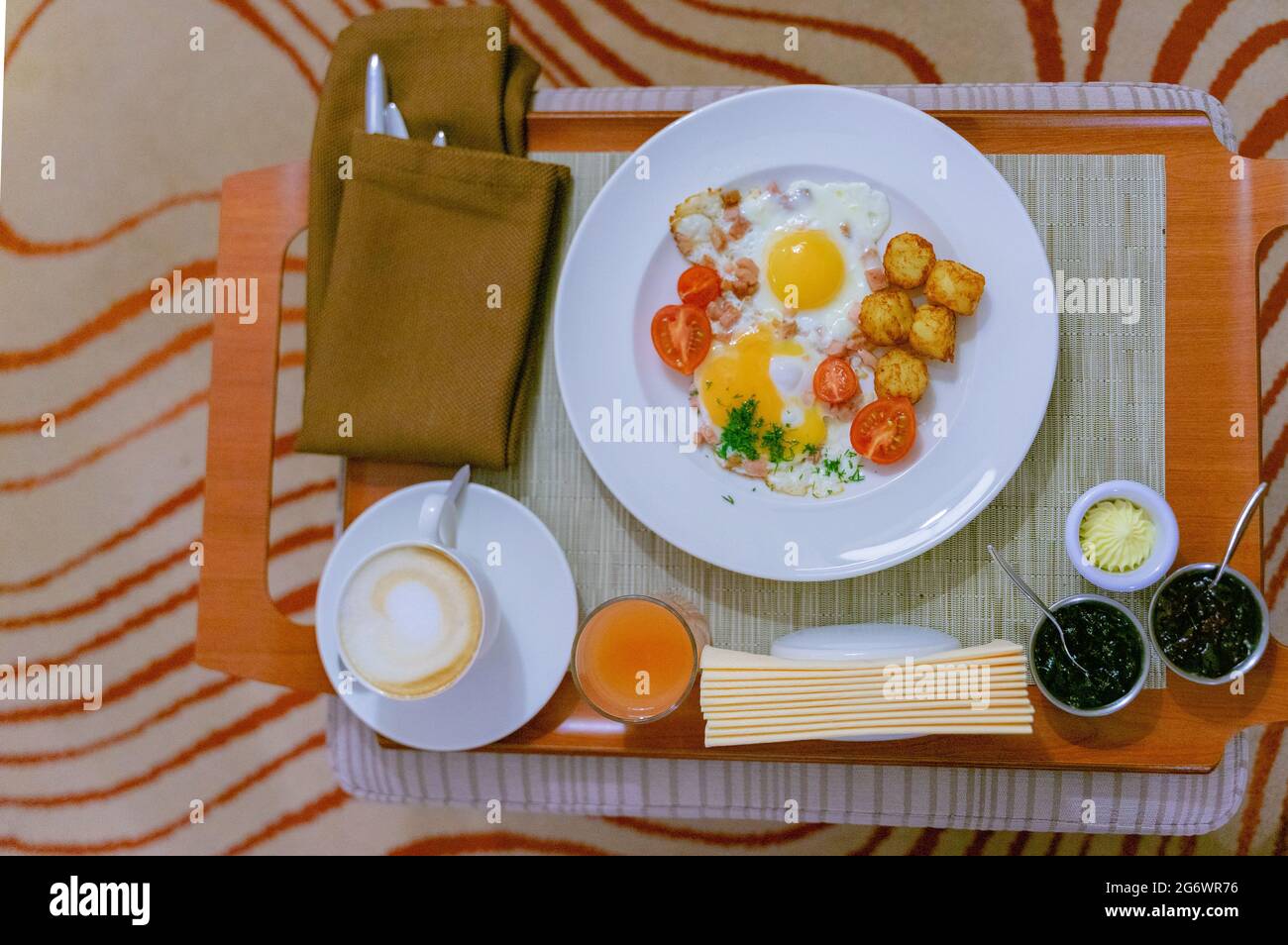 Uova fritte con prosciutto e pomodori, cappuccino, succo di frutta, marmellate, burro servito su un vassoio come colazione continentale in hotel. Foto Stock