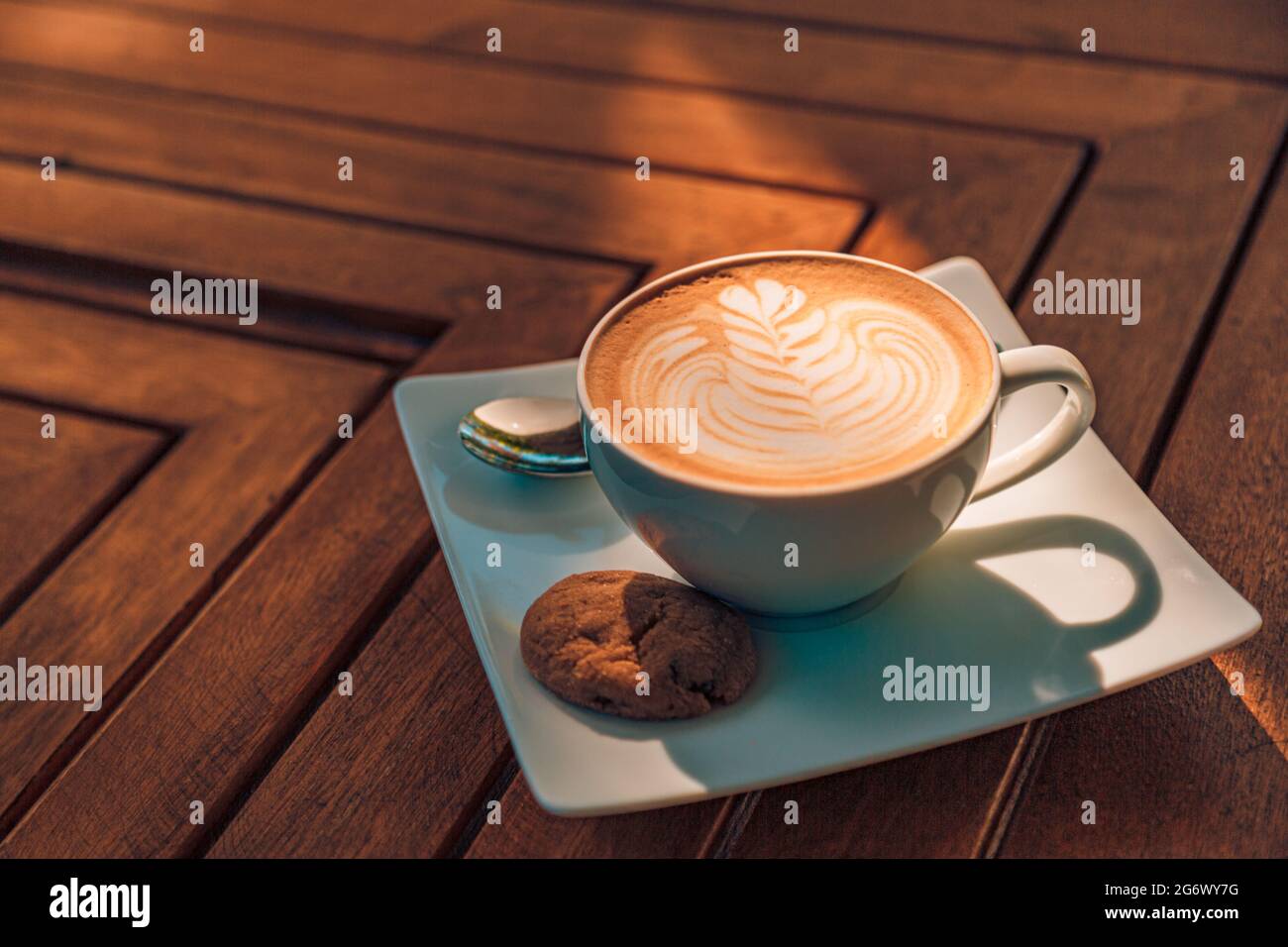 Latte art in cappuccino caffè tazza al tavolo caffè. Primo piano di rosetta fiore disegno in schiuma. Primo piano della tazza da caffè calda bianca con forma a cuore Foto Stock