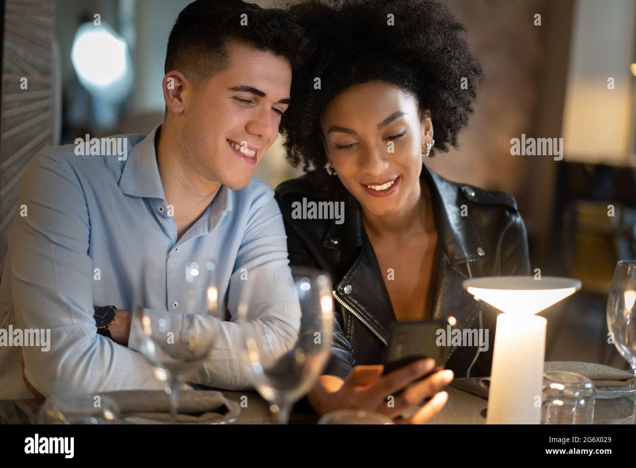 Una coppia di giovani interrazziali seduti su un tavolo da ristorante e guardando i contenuti dei social network sullo smartphone. Persone che utilizzano il concetto di tecnologia. Foto Stock