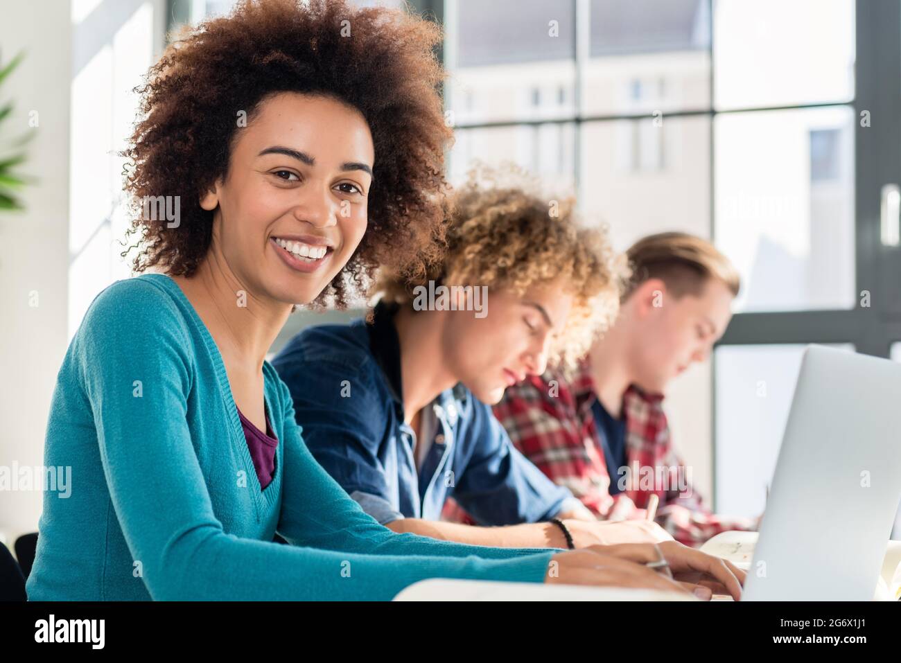 Ritratto di un allegro African American studentessa guardando la fotocamera mentre è seduto alla scrivania in aula di una prestigiosa università Foto Stock