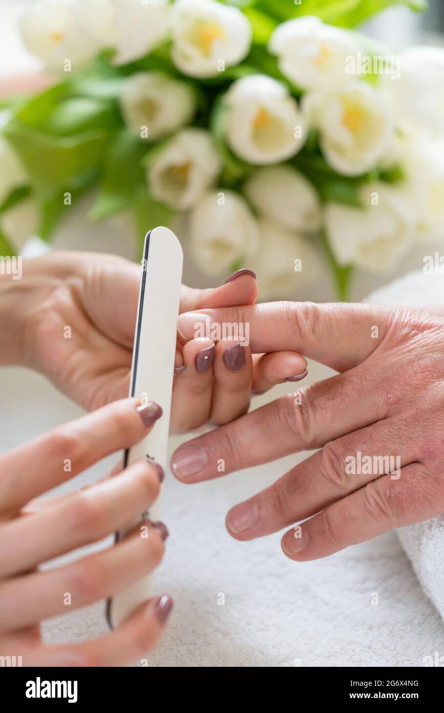 Close-up delle mani di un qualificato manicurist deposito i chiodi di una giovane donna con un tampone di bianco in un quartiere alla moda di manicure Foto Stock