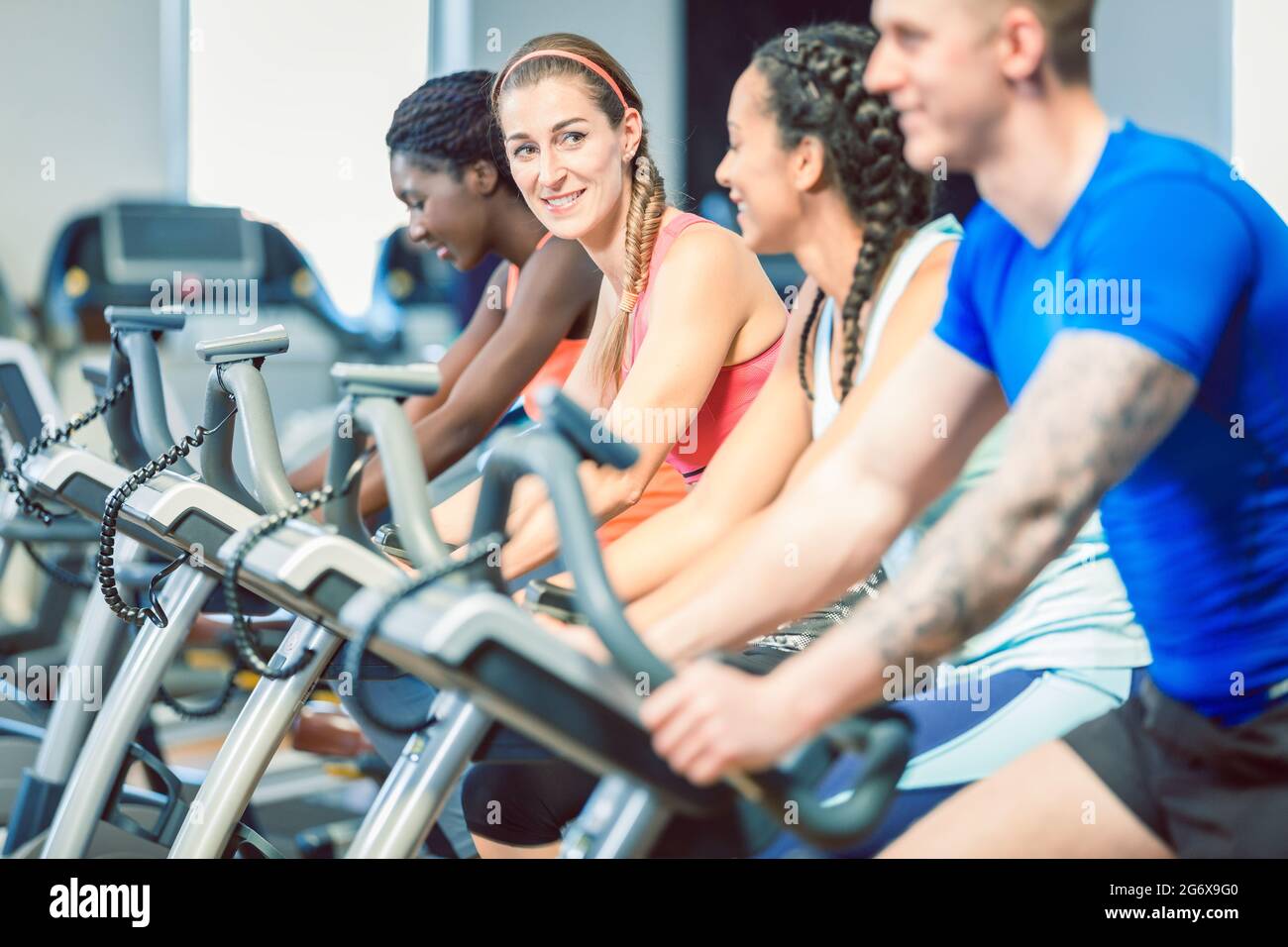 bruna bella donna sorridente mentre si pedalava su una moderna bicicletta fitness durante la lezione di spinning di gruppo in palestra Foto Stock