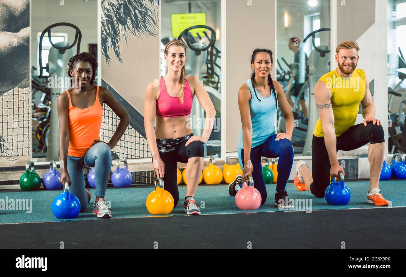 Lunghezza completa di quattro giovani e belle persone determinate che tengono kettlebells mentre si esercita l'oscillazione russa durante la classe di allenamento funzionale alla g Foto Stock