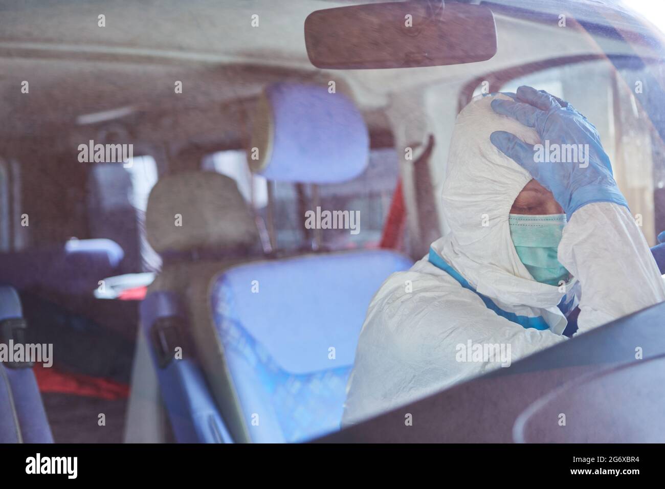 Un paramedico esausto in indumenti protettivi fa una pausa nell'ambulanza durante la pandemia del coronavirus Foto Stock