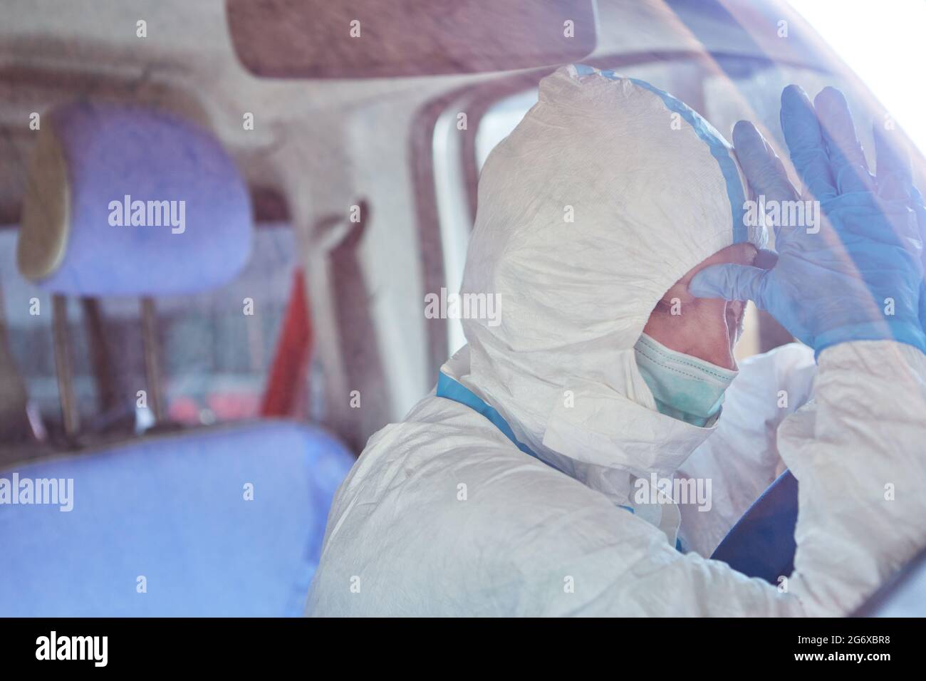 Stanco paramedico in ambulanza in indumenti protettivi dietro il volante prende una pausa dalla pandemia del coronavirus Foto Stock