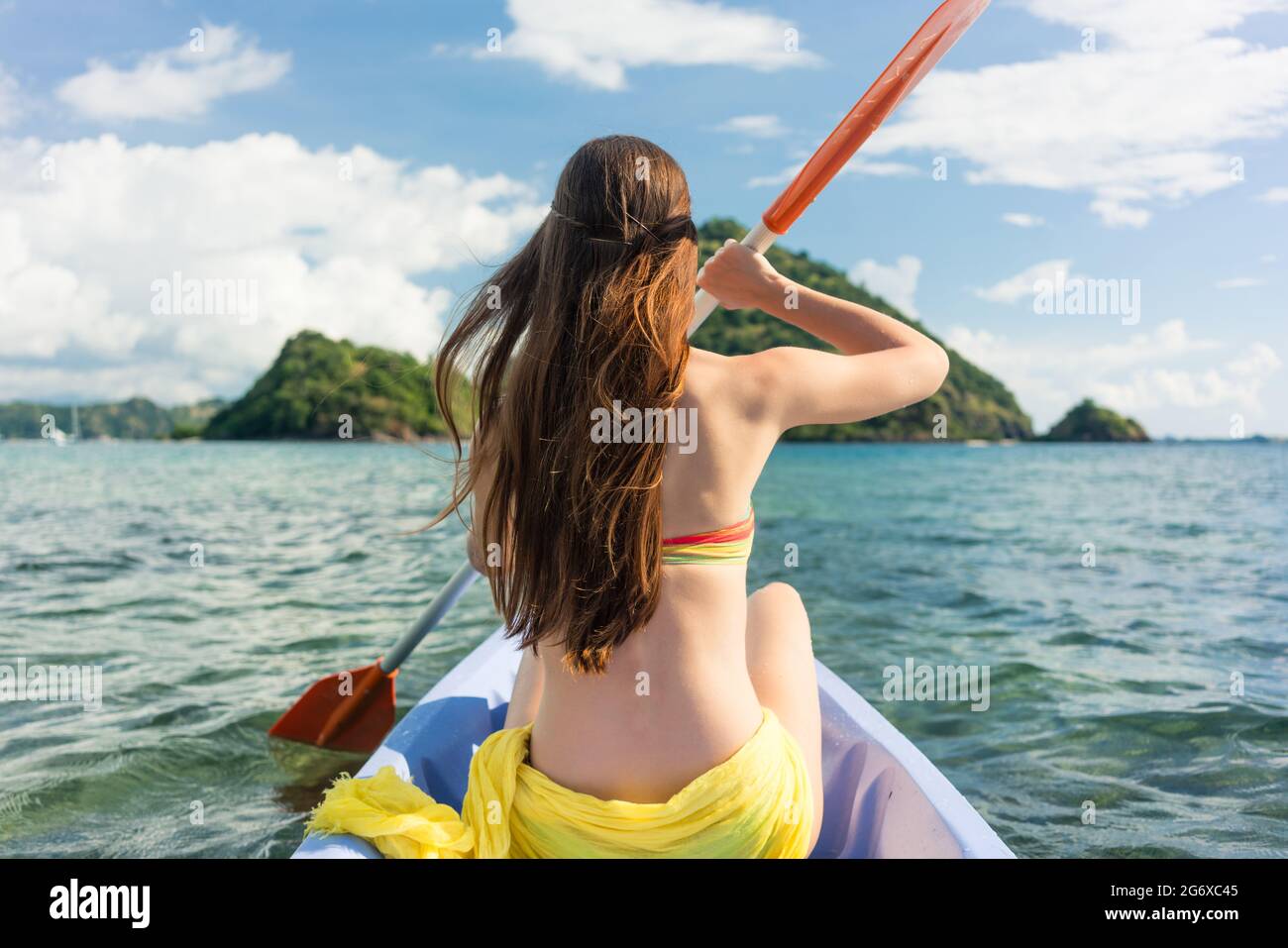 Vista posteriore di una giovane donna paddling con un doppio-bladed pagaiare in canoa sul mare durante le vacanze estive in sull isola di Flores, Indonesia Foto Stock