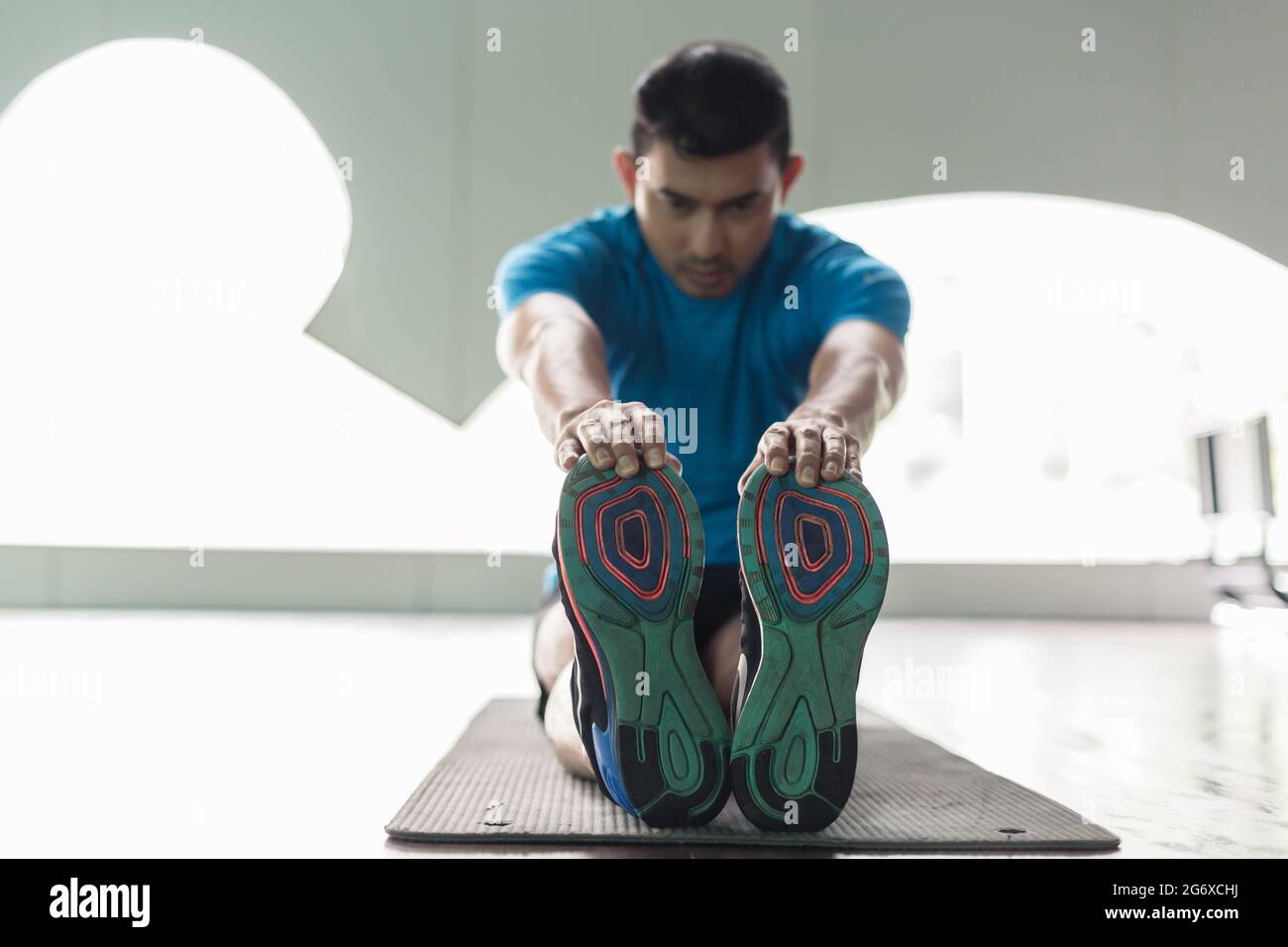 Ad angolo basso a lunghezza piena vista di un uomo seduto sul tappeto di esercizio mentre si tocca le sue dita dei piedi durante la routine di stretching in palestra Foto Stock