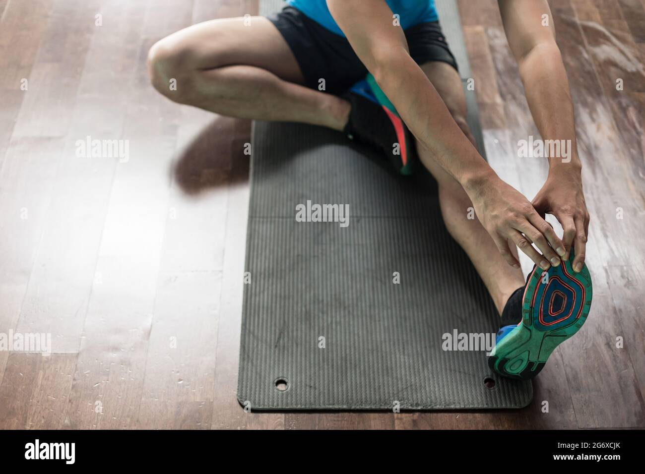 Ad alto angolo di visione delle mani di un uomo, toccando le sue dita dei piedi dalla posizione seduta come un esercizio di stretching per la flessibilità a casa o in palestra Foto Stock