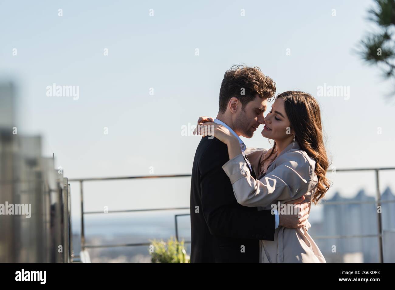 uomo che abbugge donna sorridente in cappotto sulla terrazza del ristorante Foto Stock